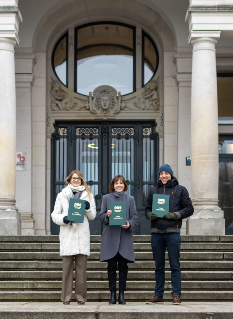 Zdjęcie przed Politechniką Gdańską, przedstawia 3 osoby z dyplomami ukończenia studiów: Agnieszka Nieznańska, Agnieszka Roman, Thomas Leyens